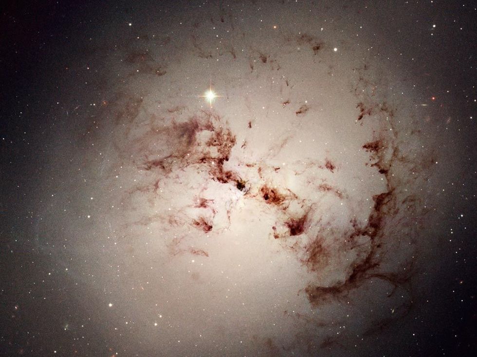 Cosmic dust nebulae orbit at the center of NGC 1316, a giant lens-shaped galaxy that formed billions of years ago when two spiral galaxies merged. Astronomers have examined clusters of red stars in NGC 1316 to determine whether this massive galaxy was indeed the subject of a major collision.